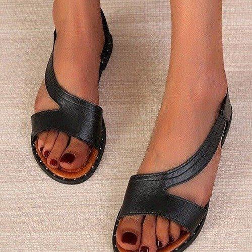 Black leather women's sandals with cross straps and stud detailing worn on bare feet with dark red nail polish