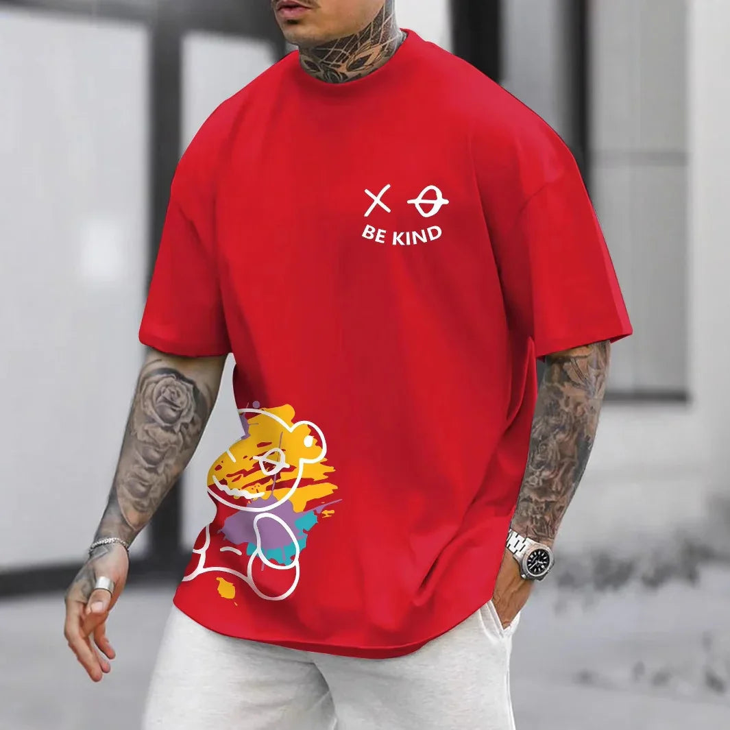 Man wearing red graphic T-shirt with colorful abstract bear and 'Be Kind' text, white pants, tattooed arms