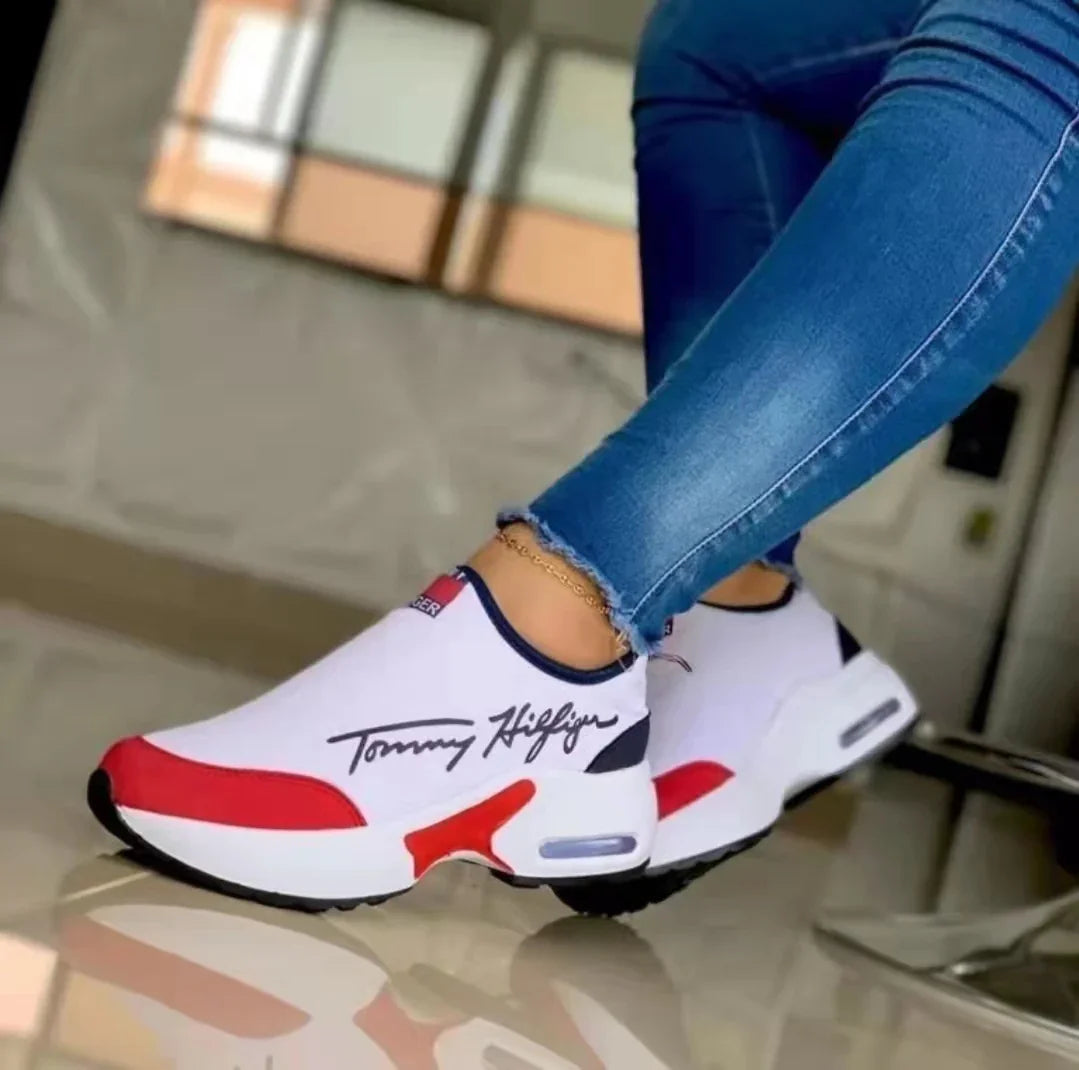 Close-up of white and red Tommy Hilfiger slip-on sneakers worn with blue jeans indoors