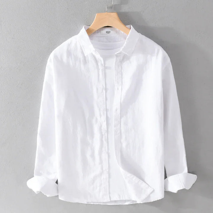 White long-sleeve linen shirt with rolled cuffs on wooden hanger against gray wall