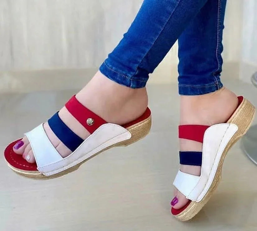 Women's open-toe wedge sandals with red, navy blue, and white straps worn with blue jeans