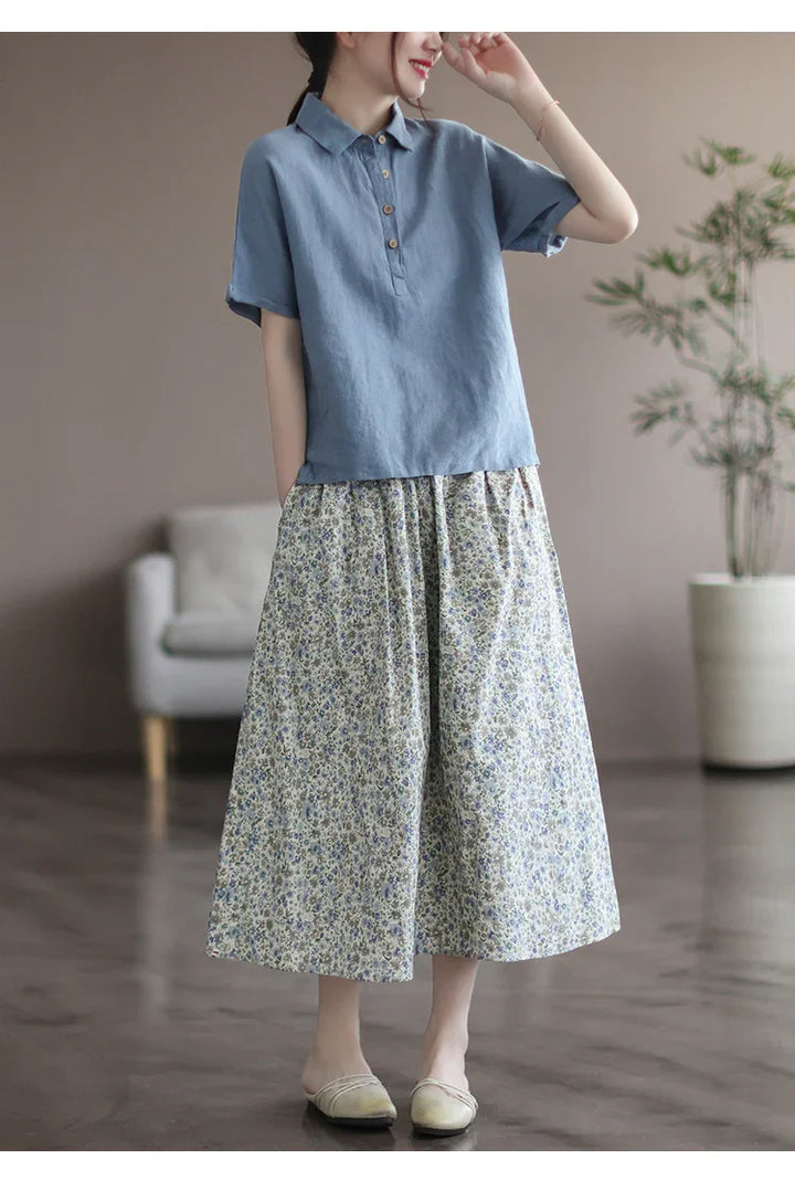 Woman wearing a casual blue button-up shirt with a floral wide skirt and cream slip-on shoes indoors