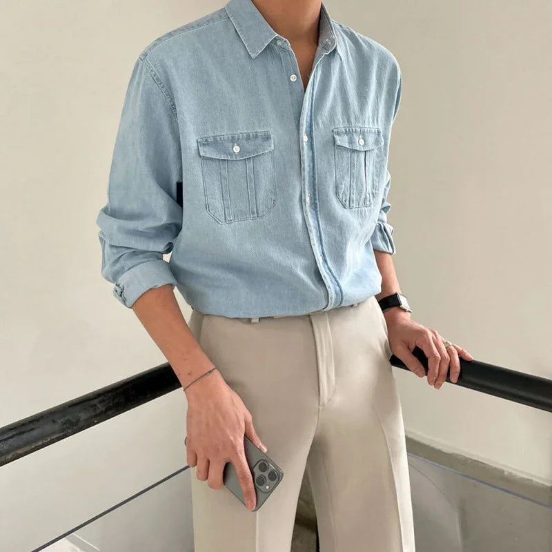 Man wearing light blue denim shirt and beige pants holding smartphone on staircase