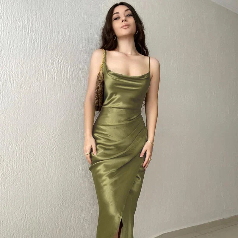 Woman in olive green satin slip dress with spaghetti straps posing against white textured wall