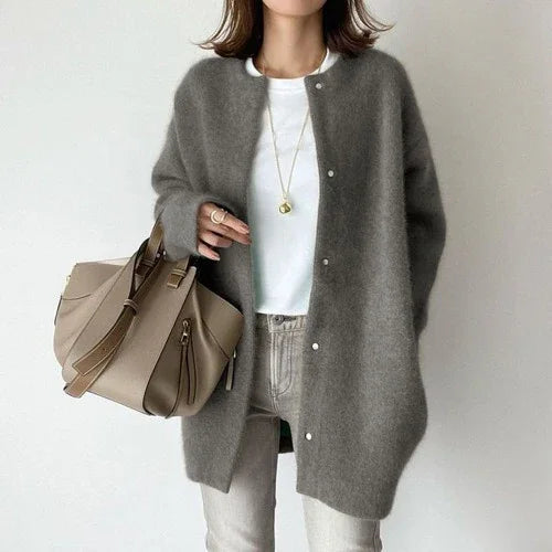Woman wearing oversized gray cardigan, white shirt, light jeans, holding beige handbag