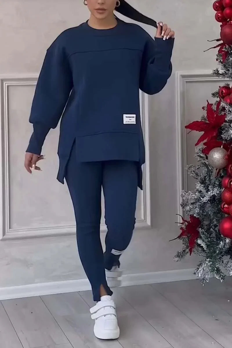 Woman wearing navy blue oversized sweatshirt and leggings with white sneakers by decorated Christmas tree