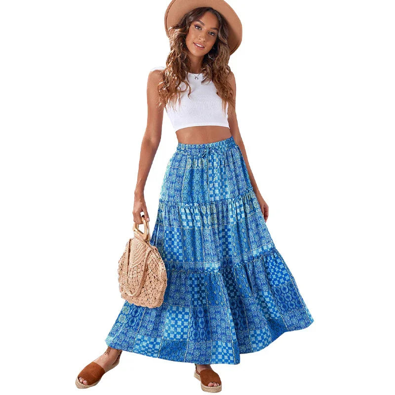 Woman wearing blue patchwork maxi skirt, white crop top, brown hat, and holding woven handbag