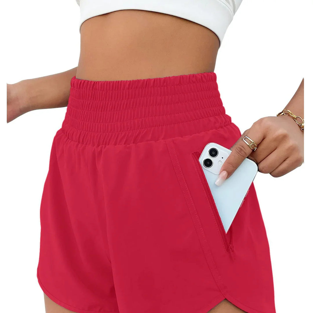 Woman wearing high-waisted red athletic shorts with zippered pocket holding white smartphone