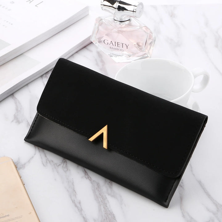 Elegant black leather and suede wallet with gold clasp on marble surface, with perfume and cup