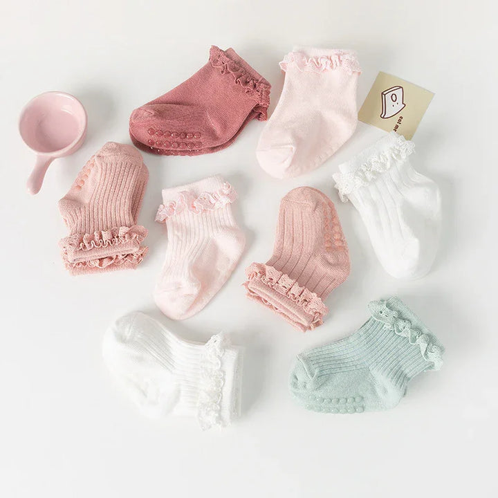 Soft pastel baby socks in pink, white, and mint with ruffled edges and silicone grips on a white background