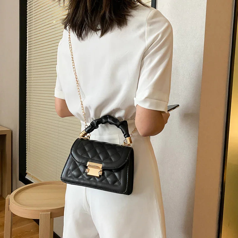 Woman in white outfit wearing a black quilted leather handbag with gold chain strap indoors