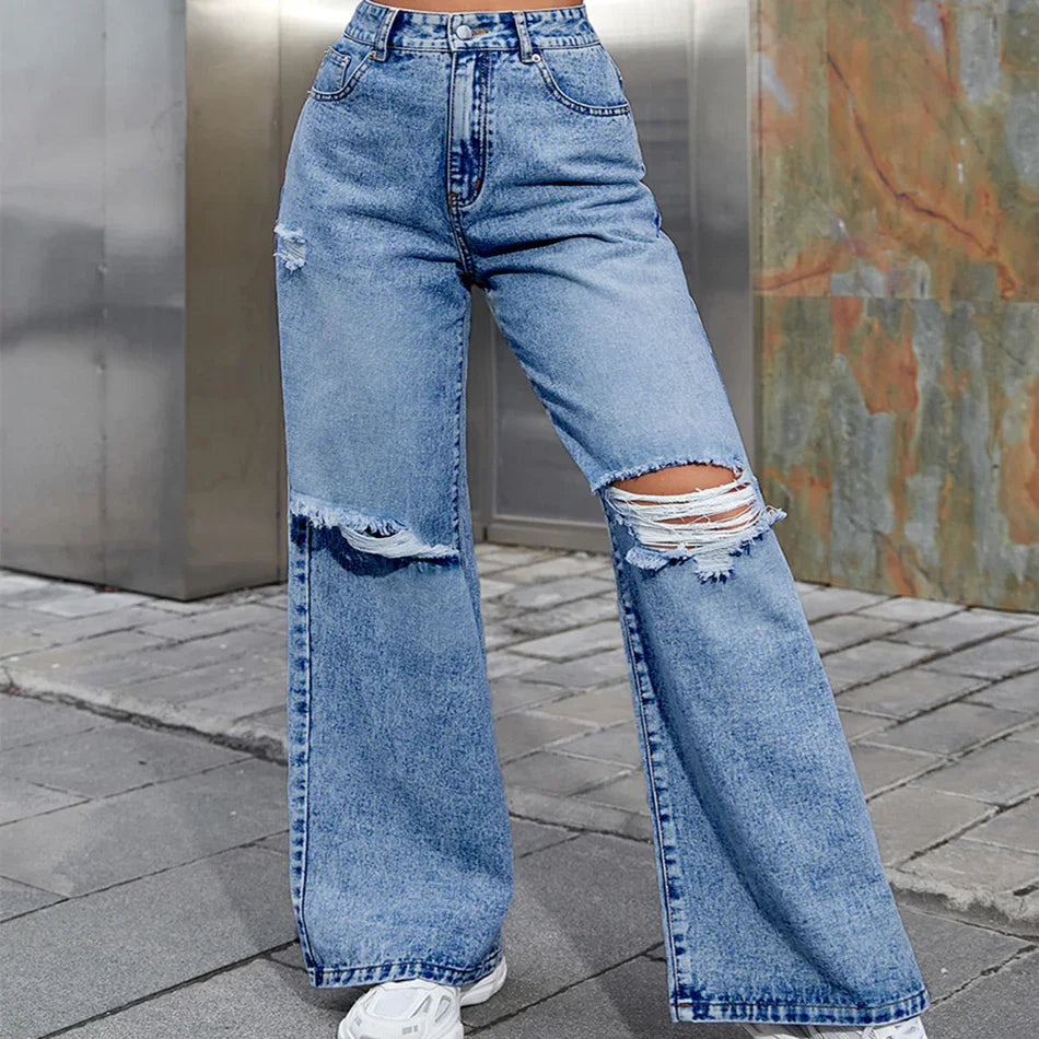 High-waisted wide-leg denim jeans with distressed rips on knee and thigh, worn with white sneakers