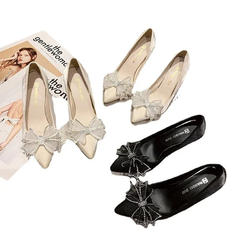 Elegant beige and black pointed toe flats with decorative bows, styled on a white background with fashion magazines