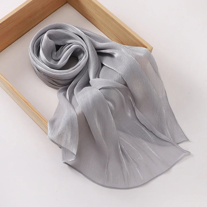 Elegant silver-gray shiny chiffon scarf rolled inside a wooden frame on a white background