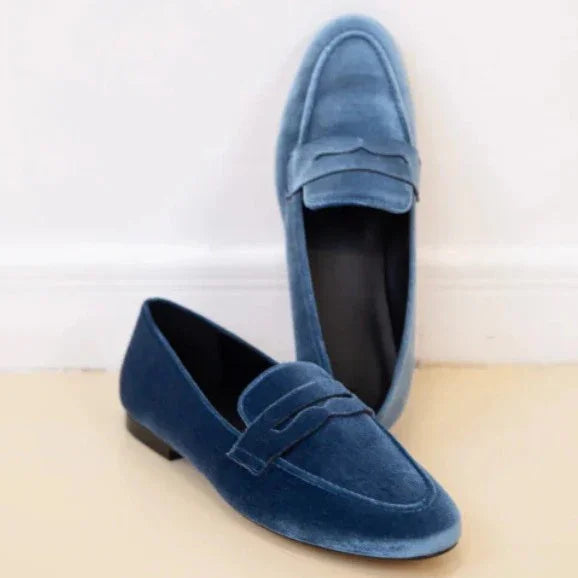 Pair of elegant blue velvet loafers on beige floor with white wall background