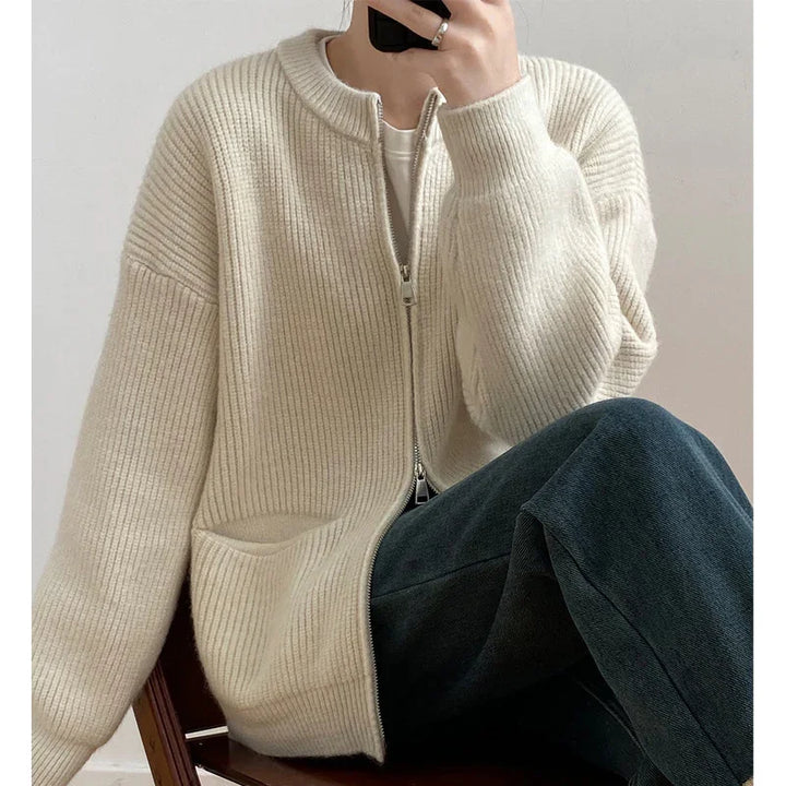 Person wearing cozy cream zip-up ribbed cardigan and dark jeans sitting on wooden chair