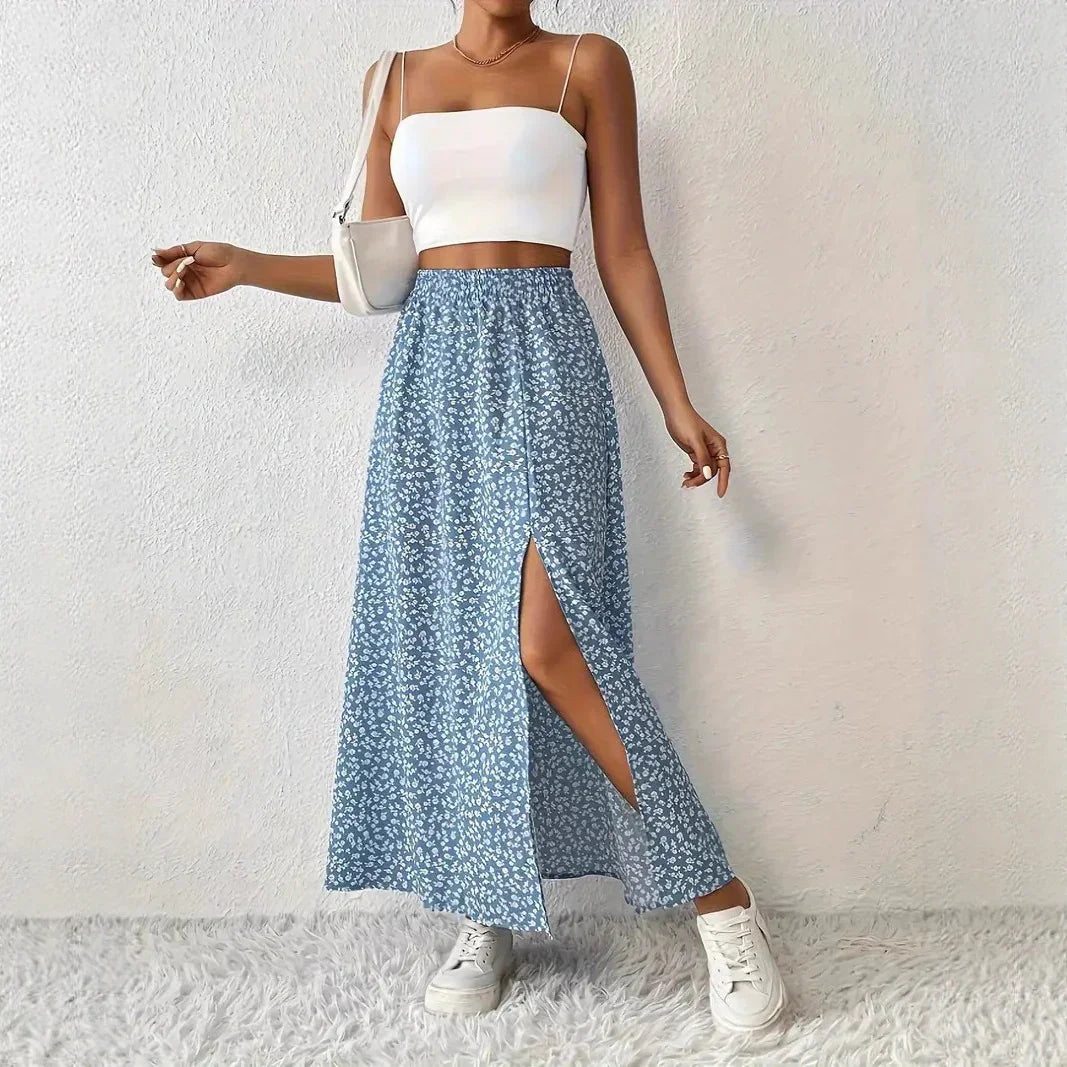Woman wearing white crop top, blue floral slit skirt, white sneakers, posing indoors on white textured background