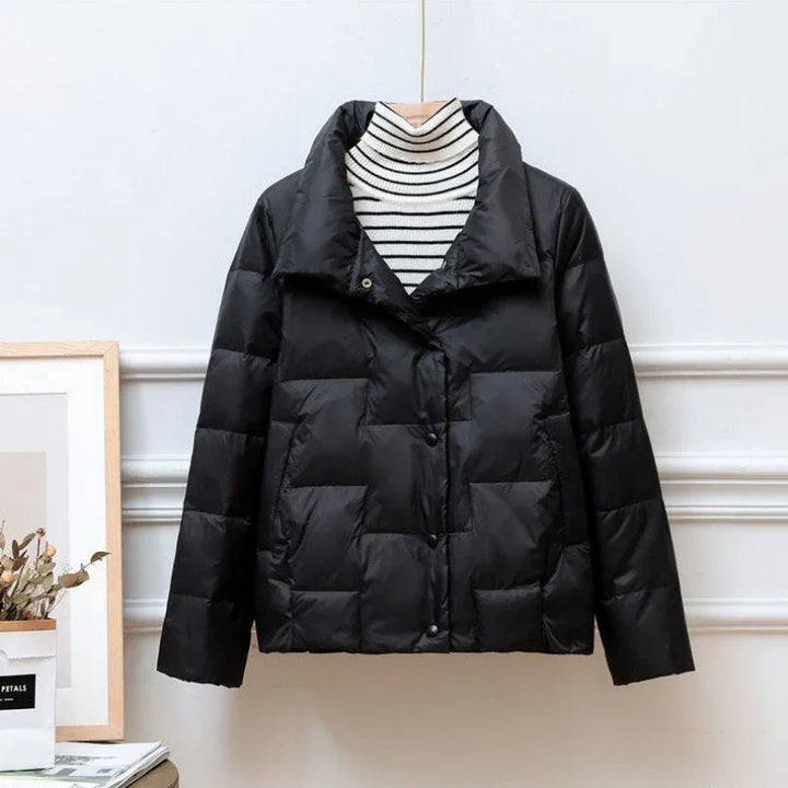Black quilted puffer jacket displayed on hanger over striped white and black turtleneck sweater
