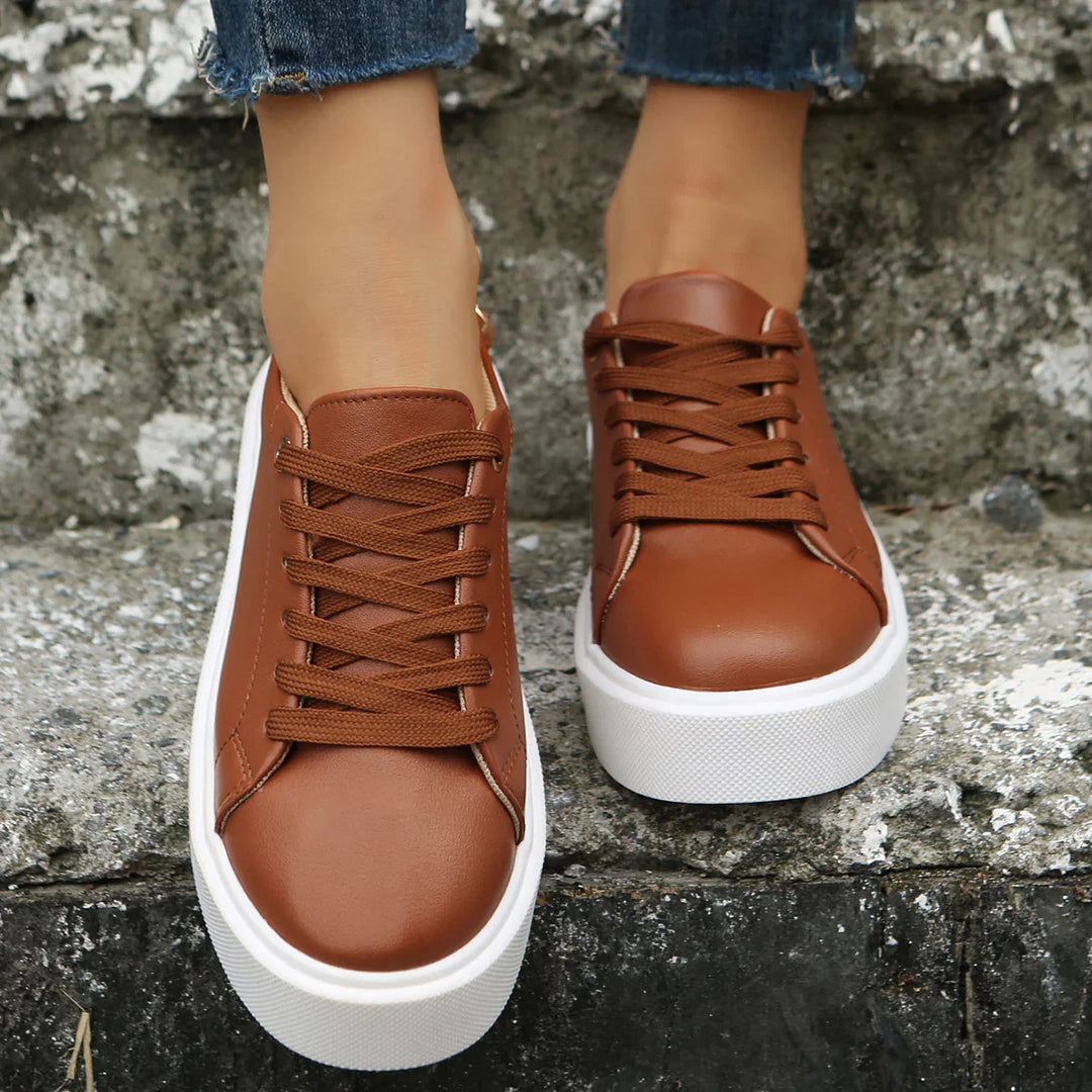 Close-up of brown leather sneakers with white platform soles worn with blue jeans on stone steps