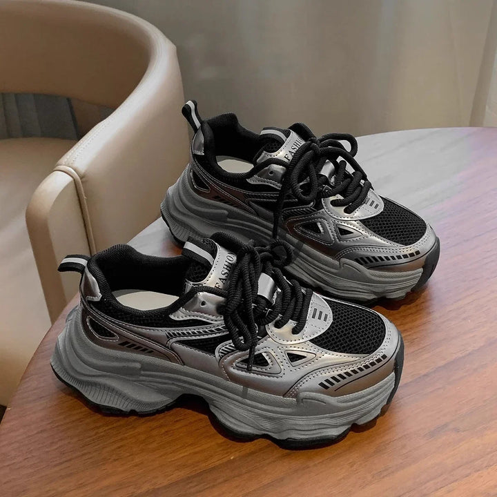 Chunky black and silver sneakers with thick soles on wooden table near beige chair