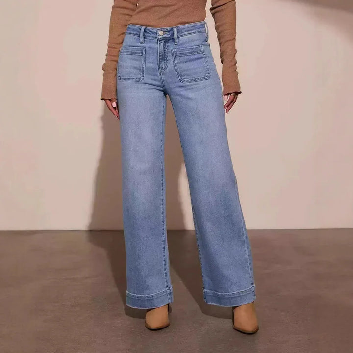 Woman wearing light blue wide-leg jeans with large front pockets and tan boots on brown floor