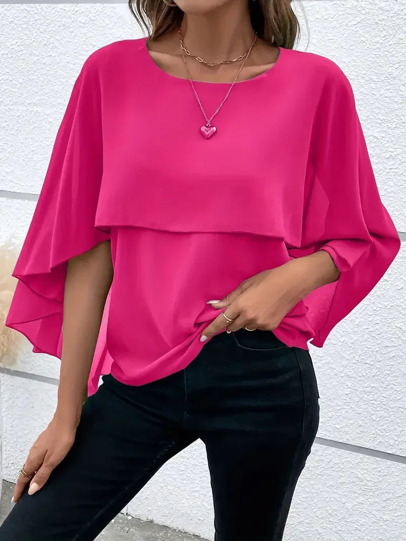 Woman wearing bright pink layered batwing sleeve blouse with black pants and heart necklace