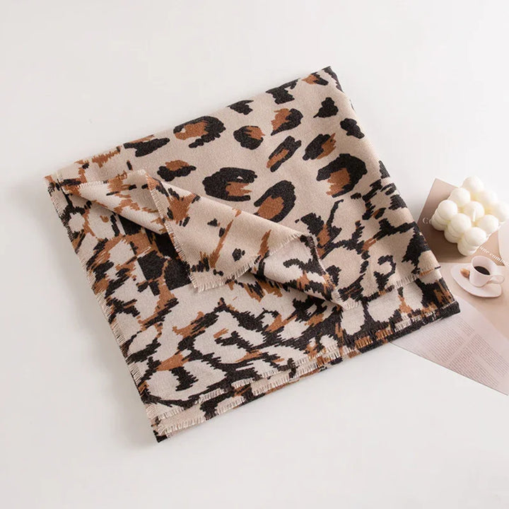 Folded leopard print scarf in beige, black, and brown on a white surface with a bubble candle and coffee cup