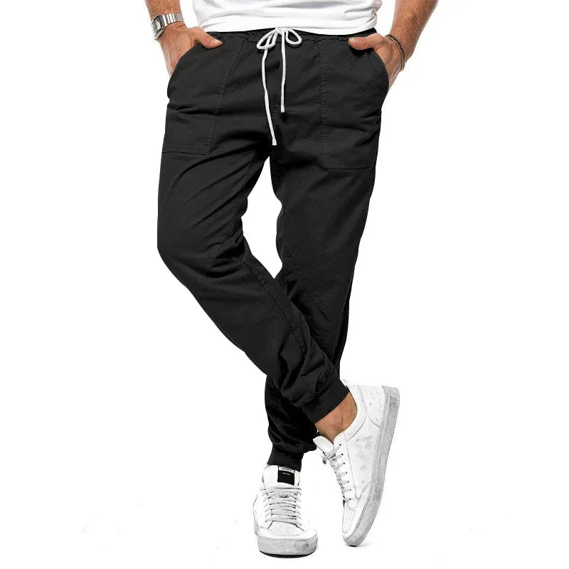 Man wearing black jogger pants with white drawstring and white sneakers on white background