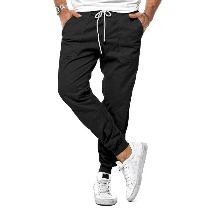 Man wearing black jogger pants with white drawstring and white sneakers on white background