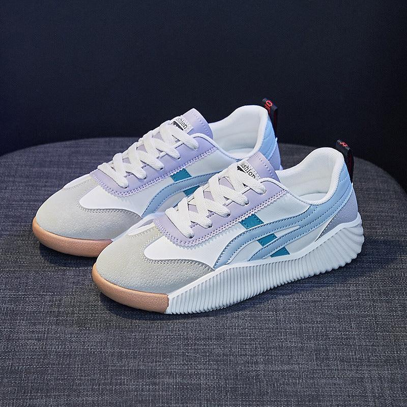 Pair of stylish white and gray casual sneakers with blue accents and gum soles on gray fabric