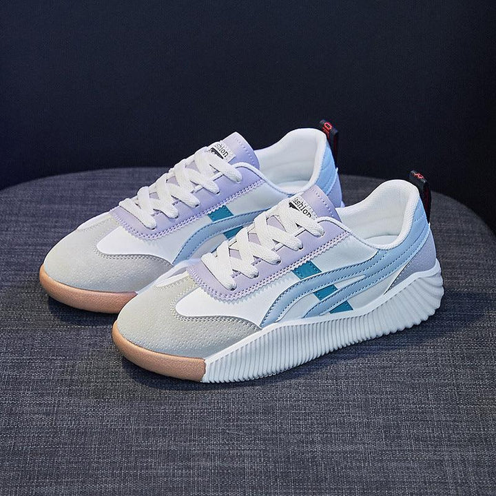 Pair of stylish white and gray casual sneakers with blue accents and gum soles on gray fabric