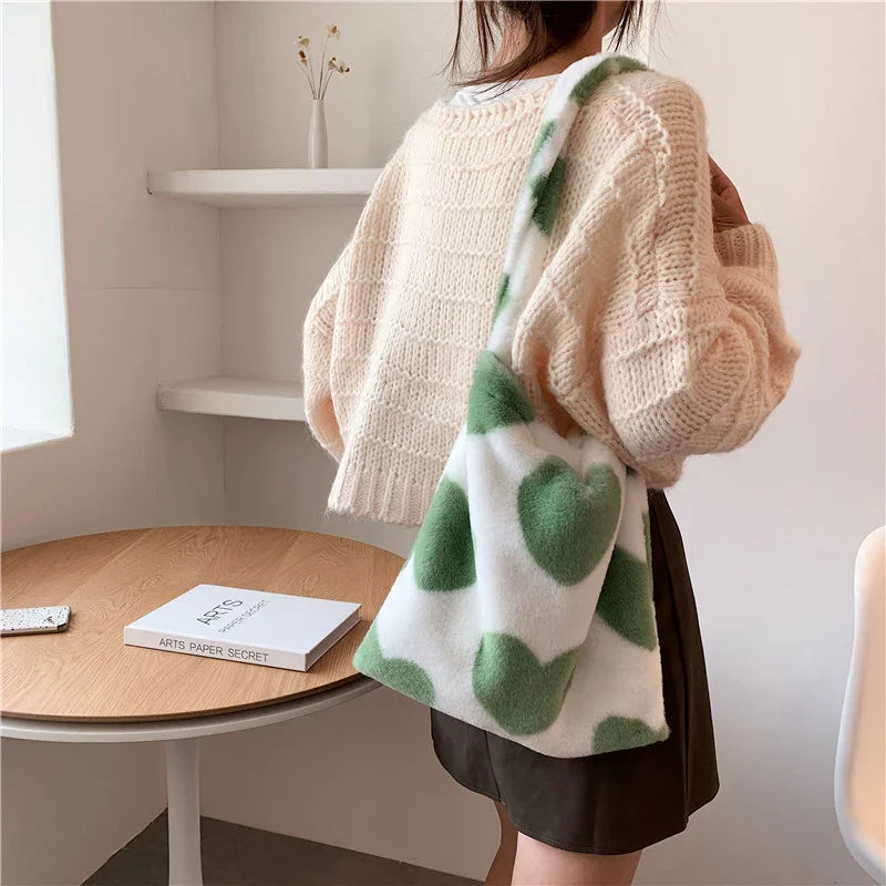 Woman wearing beige knitted sweater and dark skirt with white and green heart-patterned tote bag indoors