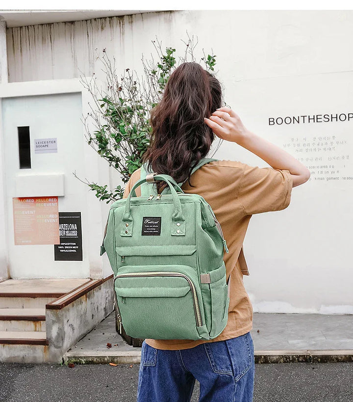 Woman with brown hair wearing a green backpack and casual outfit outdoors near white wall with Boontheshop sign
