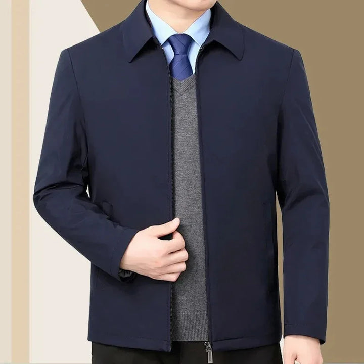 Man wearing navy blue zip-up jacket over gray sweater and blue shirt with tie