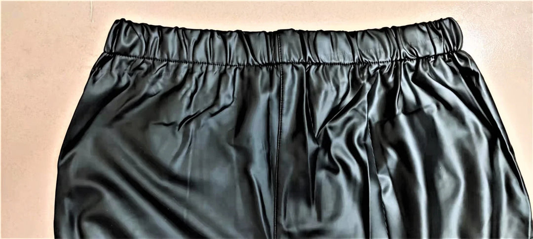 Close-up of black faux leather pants with elastic waistband on beige background