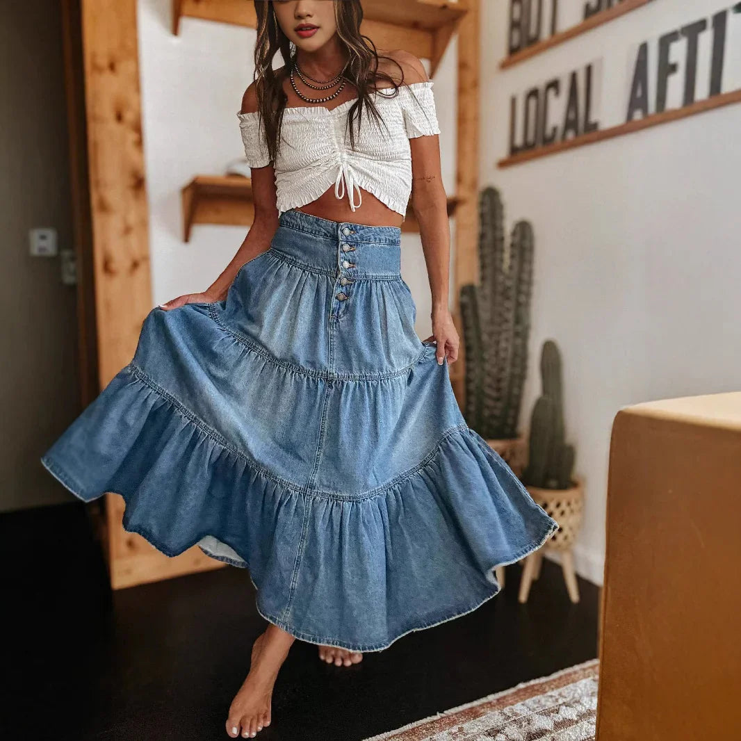 Woman twirling in a high-waisted blue denim skirt and white off-shoulder crop top indoors