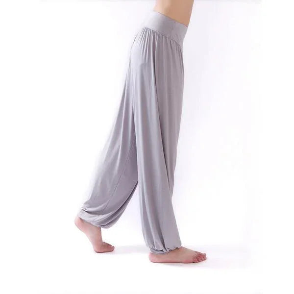 Side view of person wearing loose light gray harem pants with elastic waistband and ankle cuffs on white background