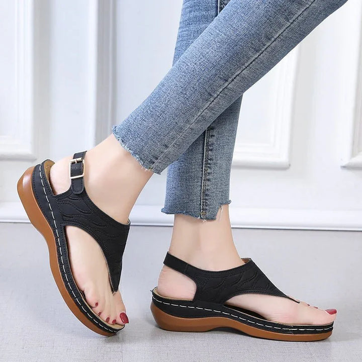 Feet wearing black leather platform sandals with brown soles and ankle straps, paired with cropped blue jeans