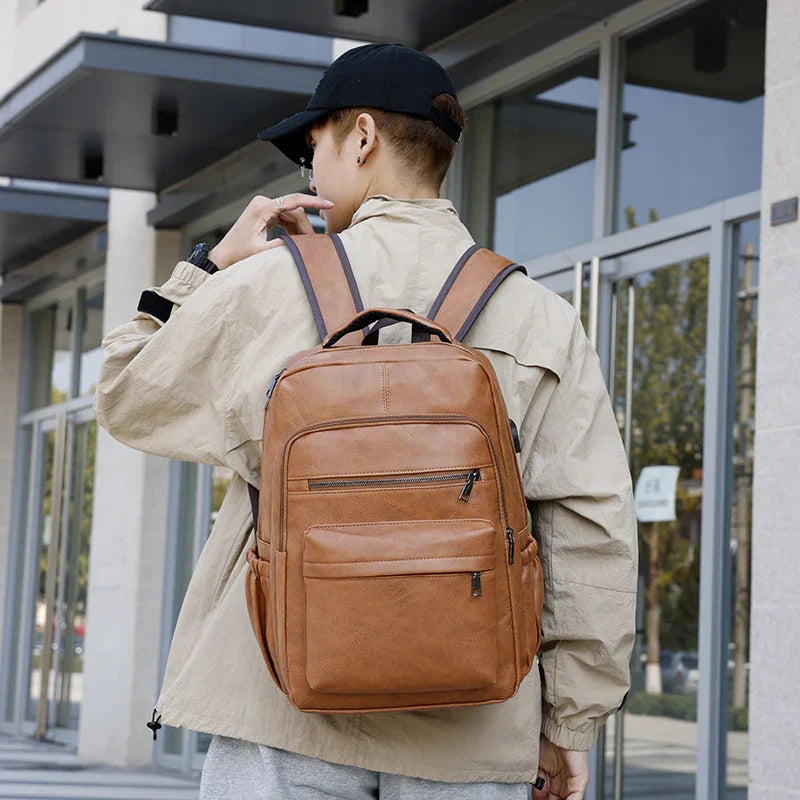 Person wearing beige jacket and black cap carrying brown leather backpack outdoors