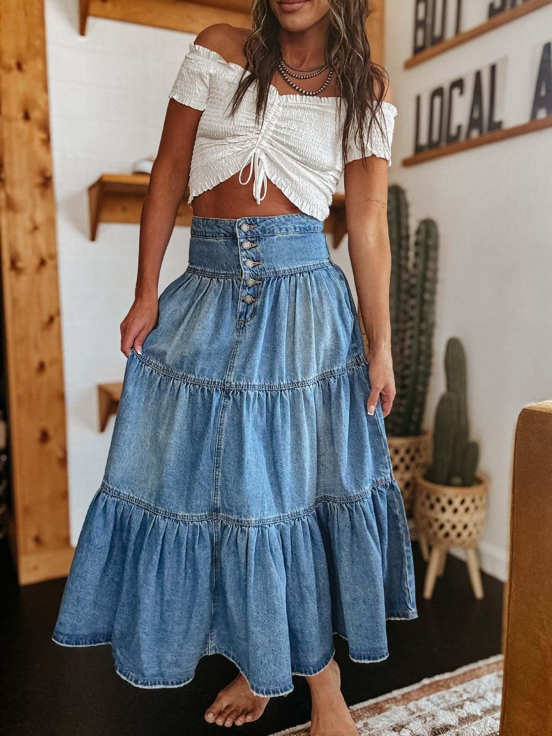 Woman wearing white off-shoulder crop top and high-waisted tiered denim maxi skirt indoors
