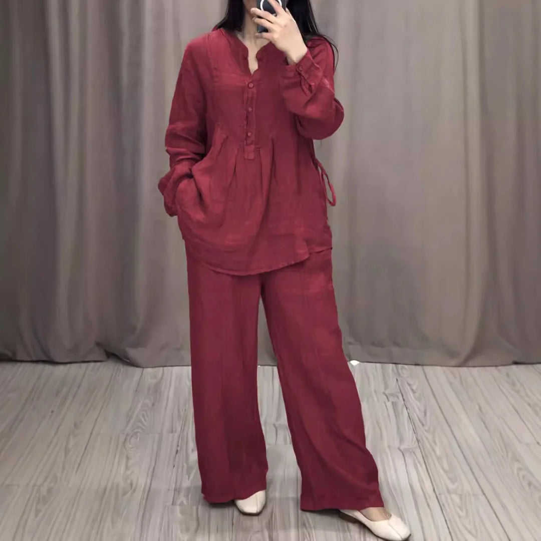 Woman wearing a loose red long-sleeve blouse and wide-leg pants standing on wooden floor