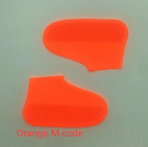 Pair of orange silicone shoe covers with textured soles on a grey background