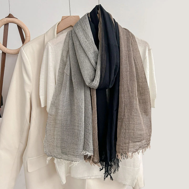 Light beige blazer and white sweater with a three-tone gray, black, and brown textured scarf on wooden hangers
