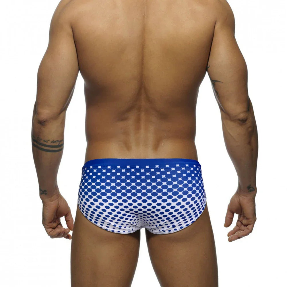 Back view of muscular man wearing blue and white polka dot swim briefs on white background