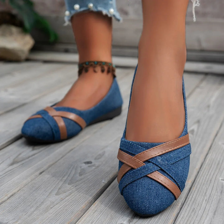 Close-up of feet wearing blue denim flats with brown cross straps on wooden floor