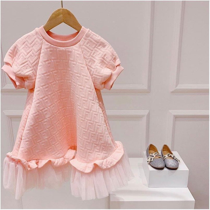 Pink textured short-sleeve baby dress with ruffled tulle hem on wooden hanger beside silver toddler shoes