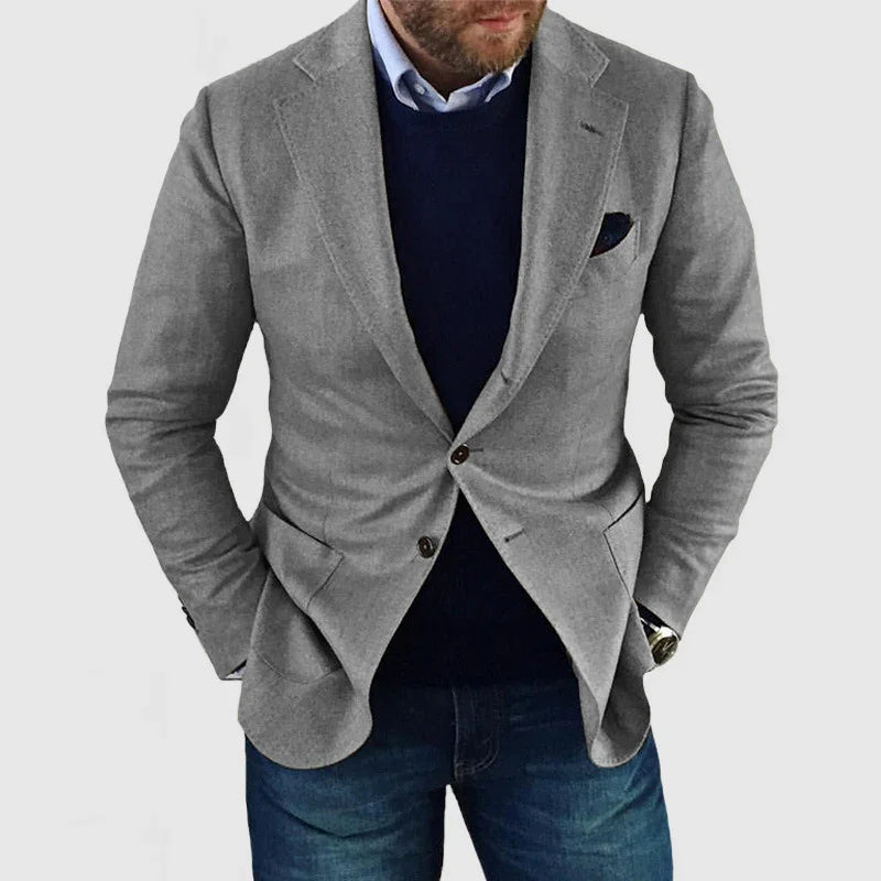 Man wearing a light grey blazer with navy sweater and blue jeans, hands in pockets