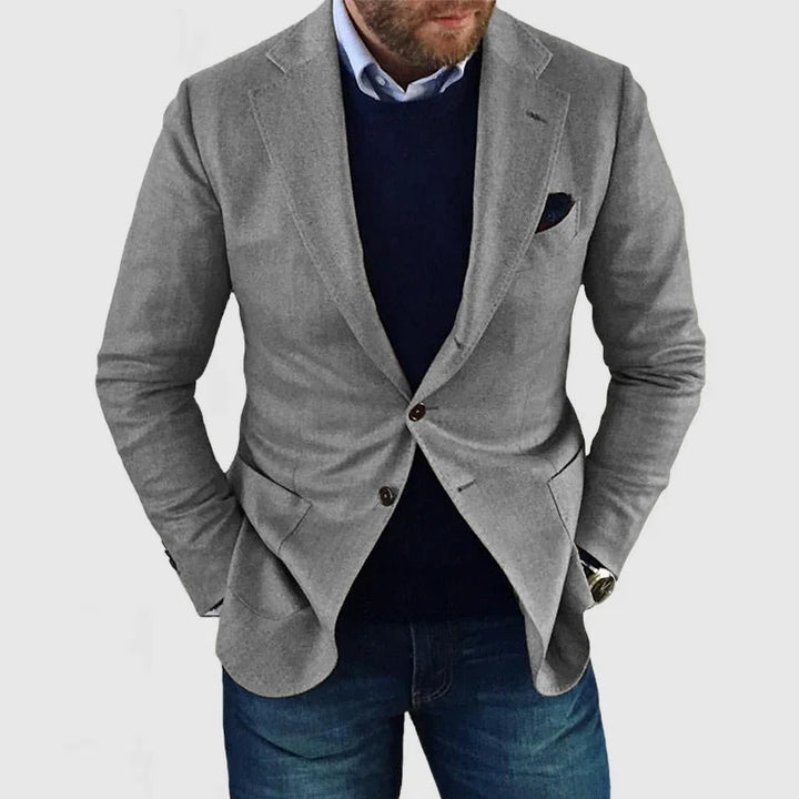 Man wearing a light grey blazer with navy sweater and blue jeans, hands in pockets