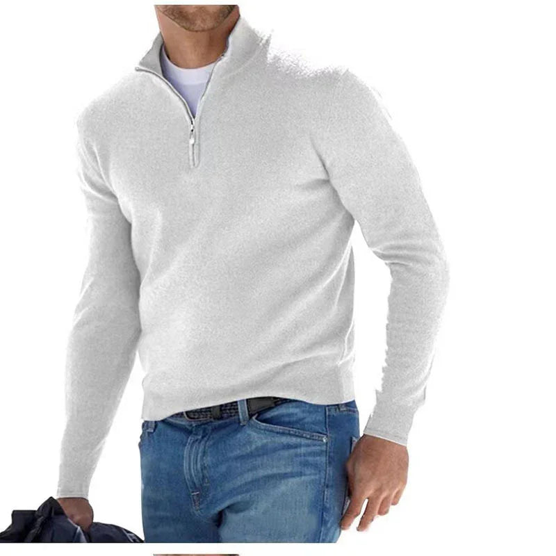 Man wearing white quarter-zip sweater paired with blue jeans holding black jacket