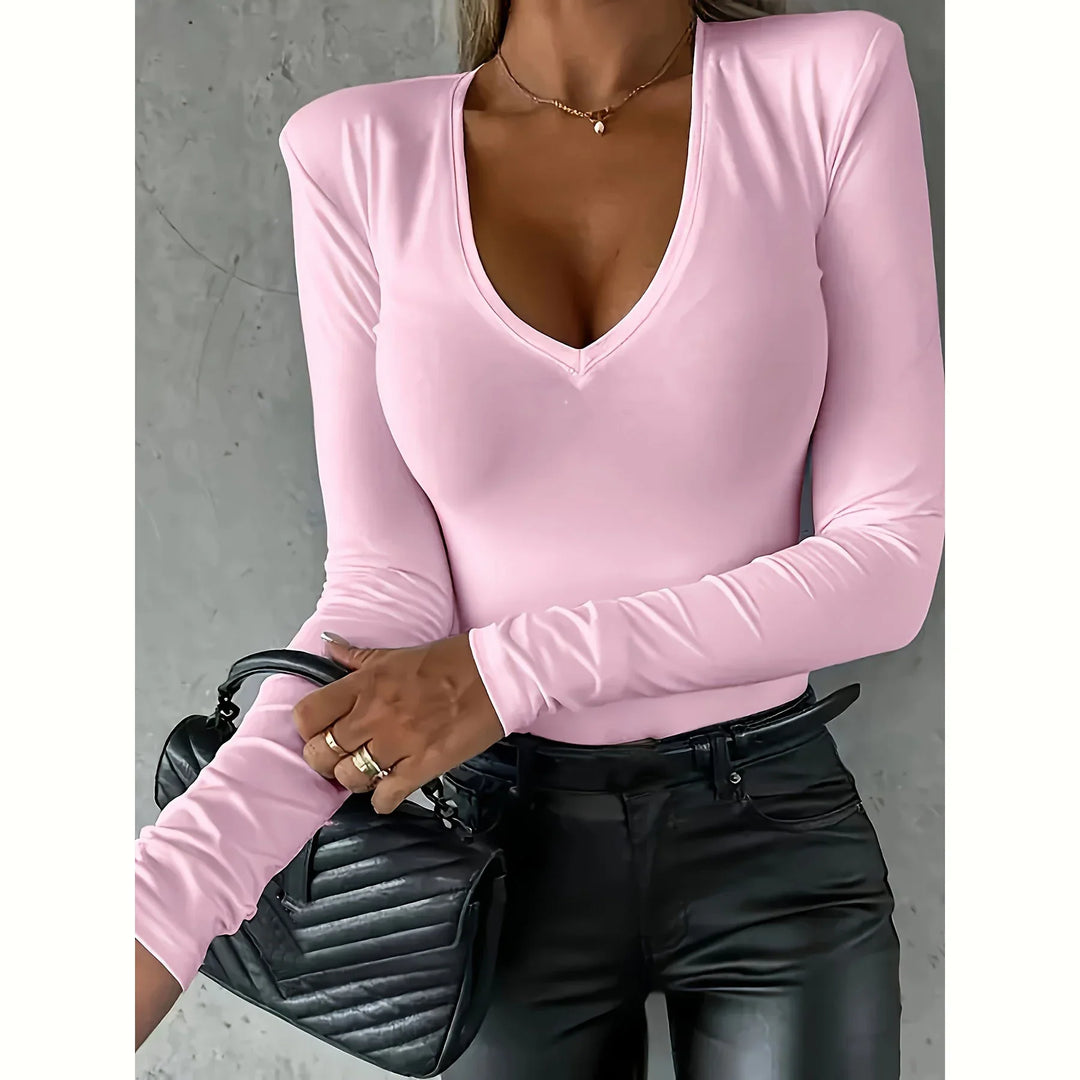 Woman wearing light pink V-neck long sleeve top paired with black leather pants and holding a black quilted handbag